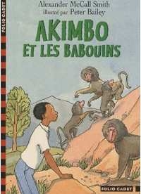 Un garçon en jeans et tee-shirt blanc, de profil, s’appuie sur un rocher et admire de près un babouin. En arrière plan, une famille de babouins joue dans les rochers.  