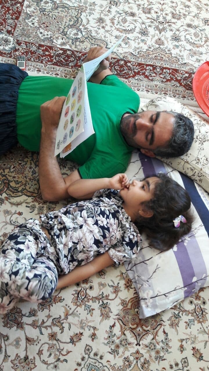 Un père lisant à sa fille, tous deux couchés sur le tapis.