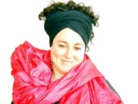 Portrait de Nadine Touma. Elle porte un turban noir dans les cheveux et un drapé rose autour du buste