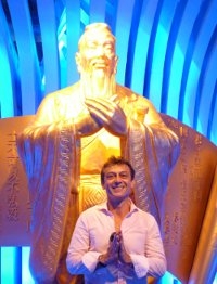 Jean-Luc Schneider pose devant la statue dorée de Confucius