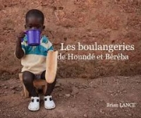 Un petit garçon tient à ses mains un pain et une tasse, assis sur un tabouret. 