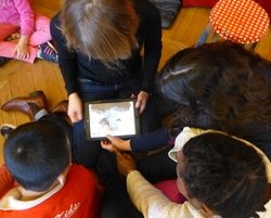 Vue d'en haut - 4 enfants en train de regarder une tablette, têtes penchées.